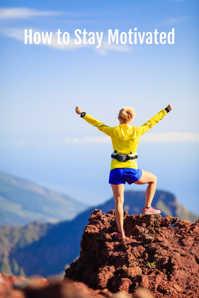 how to stay motivated - photo shows Climbing hiking or trail running woman in mountains with arms outstretched at the top of the mountain