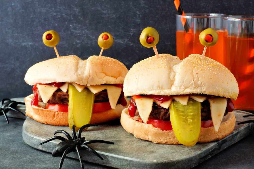 hamburgers made to look like monsters with toothpicks and olives as eyes in the bun and a pickle slice tongue hanging out
