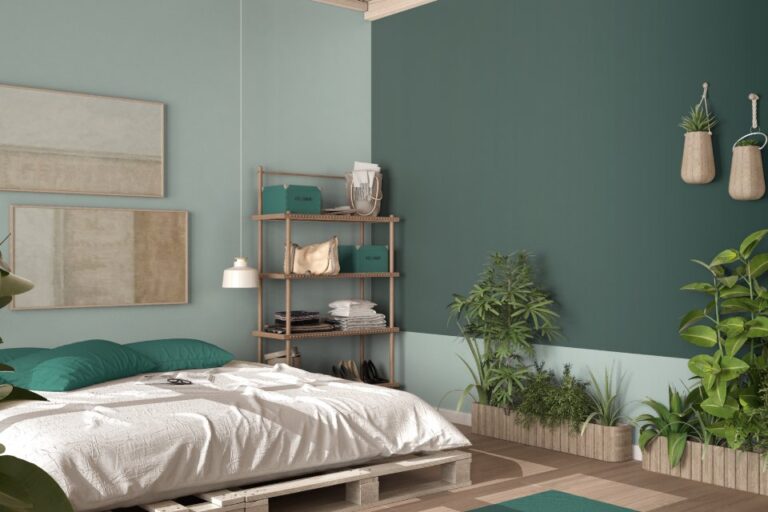 A white bed with green pillows sits on white wood pallets while surrounded by green plants and green walls.