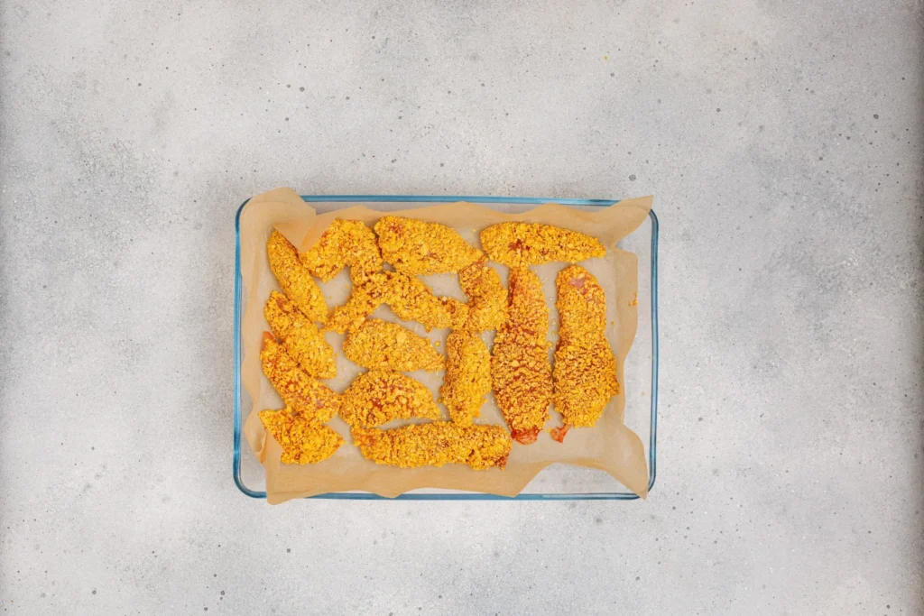 Breaded Dorito chicken tenders arranged on a parchment-lined baking tray before baking.