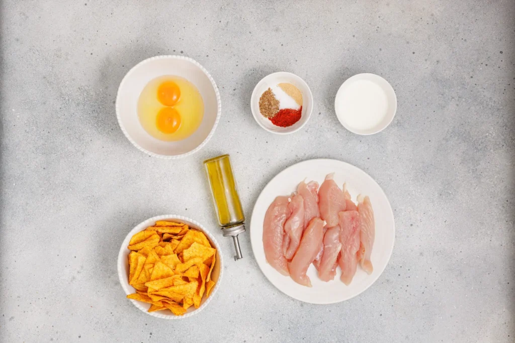 Overhead view of ingredients for Dorito chicken tenders, including eggs, spices, milk, Doritos, and raw chicken.