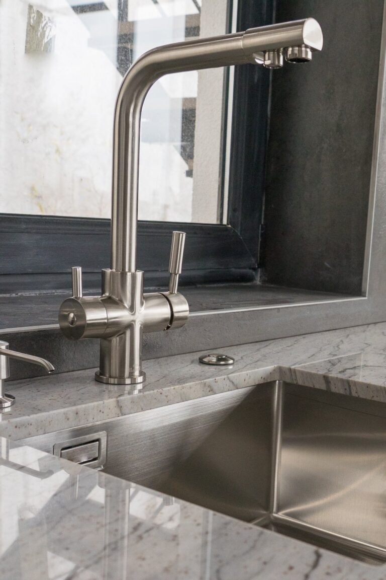 A marble countertop in a kitchen with a stainless steel undermount sink near a window with a black frame.
