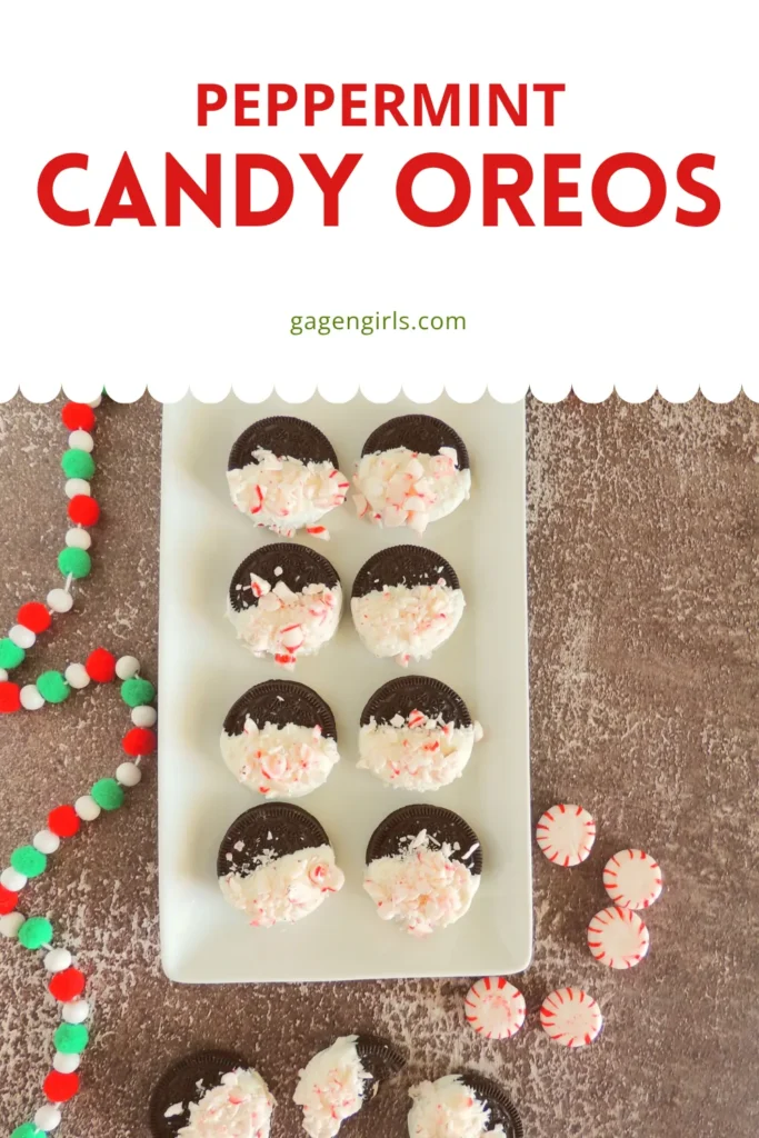 Overhead view of Oreo cookies dipped in white chocolate and topped with crushed peppermint, arranged on a white plate with festive holiday garland.