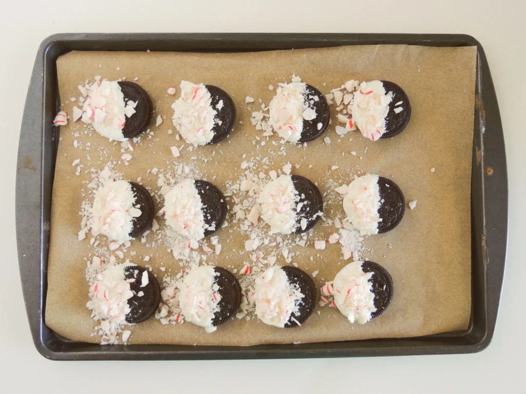 White chocolate-dipped Oreos sprinkled with crushed peppermint candy on a baking sheet.