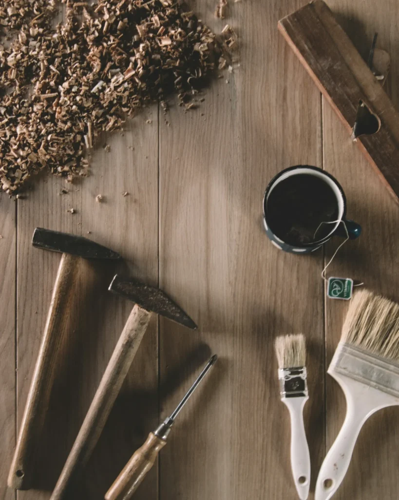 Hammers, brushes, and woodworking tools arranged on a wooden surface next to a cup of tea.
