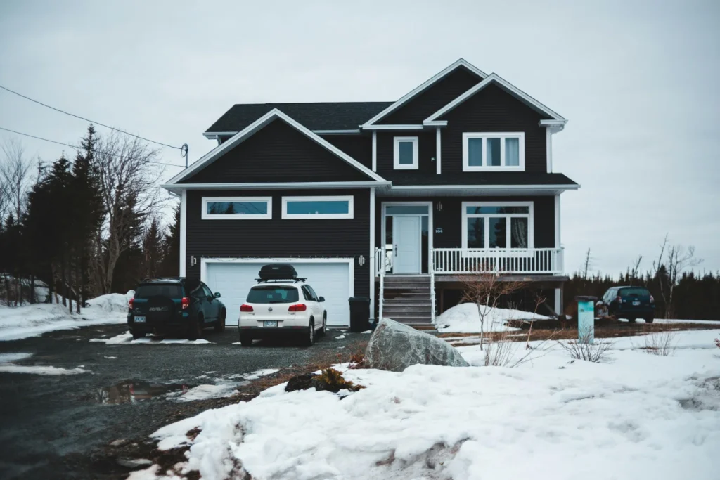 Two-story family home with a snow-covered driveway and parked cars in winter