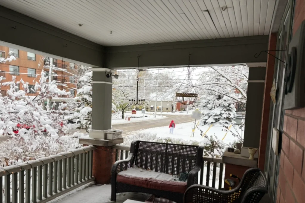 Snow-covered front porch with wicker seating and trees blanketed in fresh winter snow.