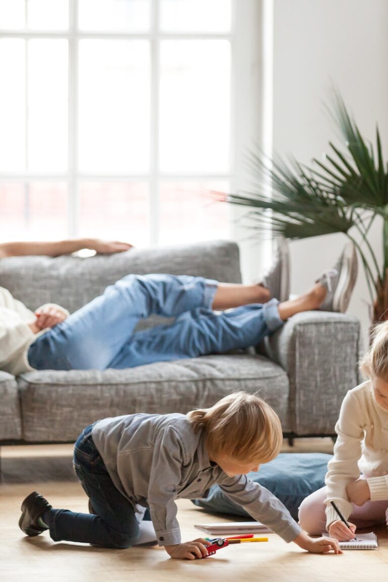 A man and a woman sit on the couch in a living room. Two children play on the floor in front of the couple.