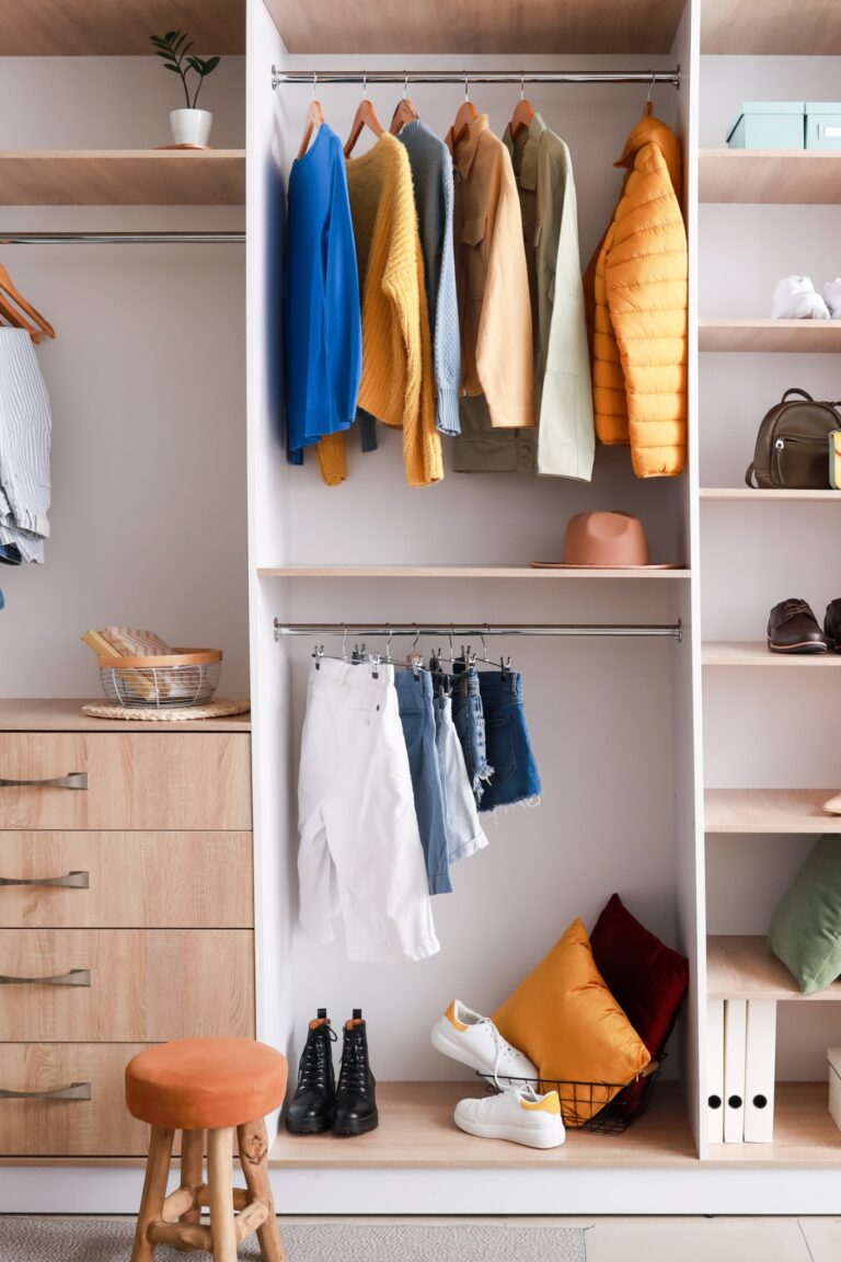 An organized open closet with shelves, hanging clothes, shoes, drawers, and decor in a bright, modern space.