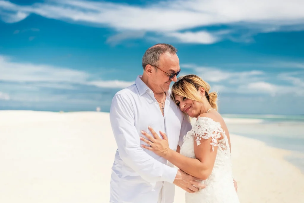 bride and groom embracing on white sand beach during intimate vow renewal