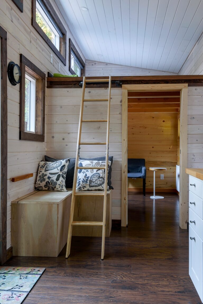 The interior of a tiny home. There is a ladder leading to a lofted bed space and a door leading to another room.