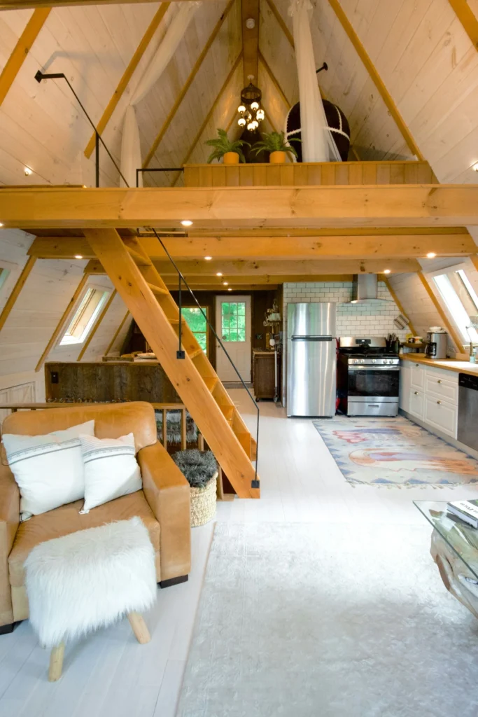 Open concept A-frame tiny house interior with loft bedroom, kitchen, and living area.