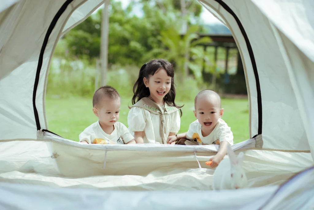 Three young children smiling and playing inside a camping tent outdoors.