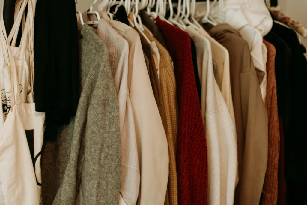 Cozy neutral-toned wardrobe with sweaters, cardigans, and layered clothing hanging neatly on white hangers.