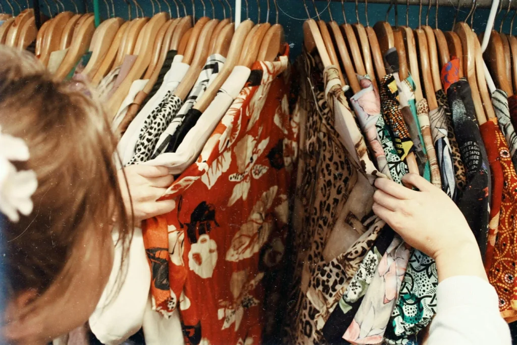 Hands sorting colorful patterned clothing on wooden hangers while organizing a wardrobe for a seasonal closet refresh.