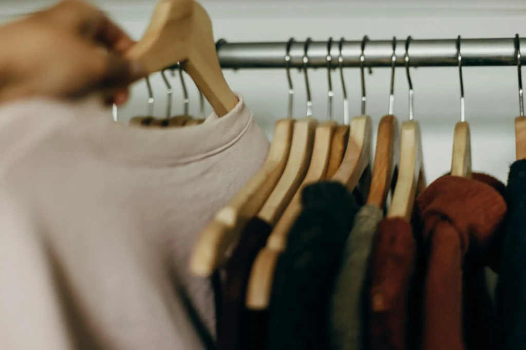 Person selecting a soft neutral sweater from a clothing rack filled with cozy seasonal layers.