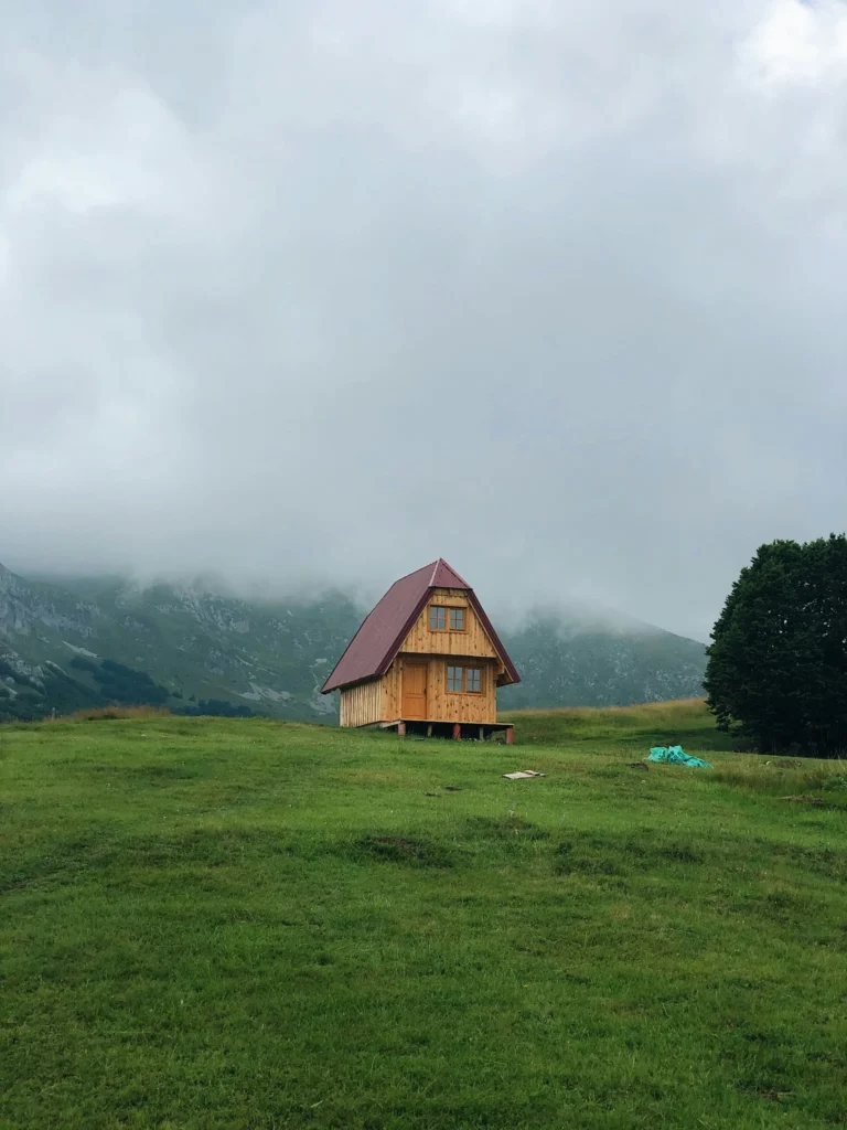Small wooden cabin sitting in a misty mountain landscape surrounded by grass.