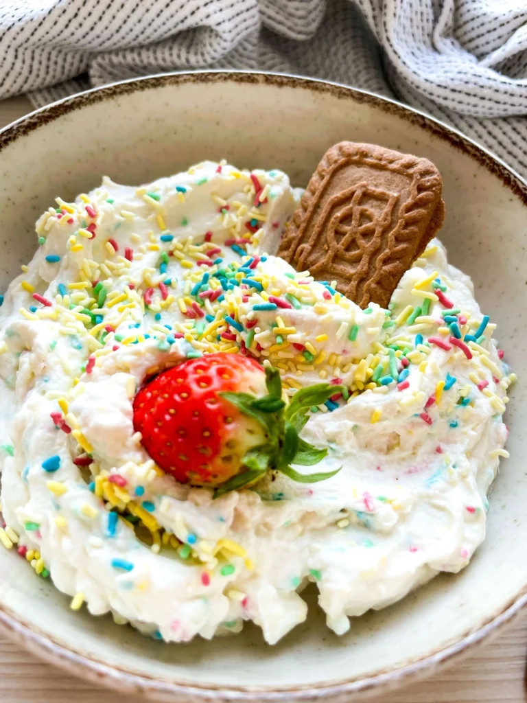 Sweet confetti dip garnished with rainbow sprinkles, a cookie, and a fresh strawberry.
