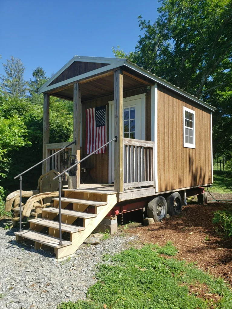 Tiny house on wheels with a front porch and wooden steps.
