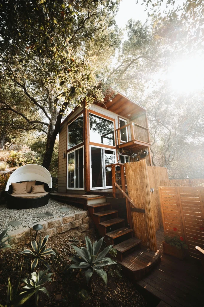 Tiny house with wooden deck and outdoor seating surrounded by trees.