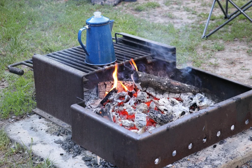 Blue enamel coffee pot heating over a campfire in a metal campground fire pit.