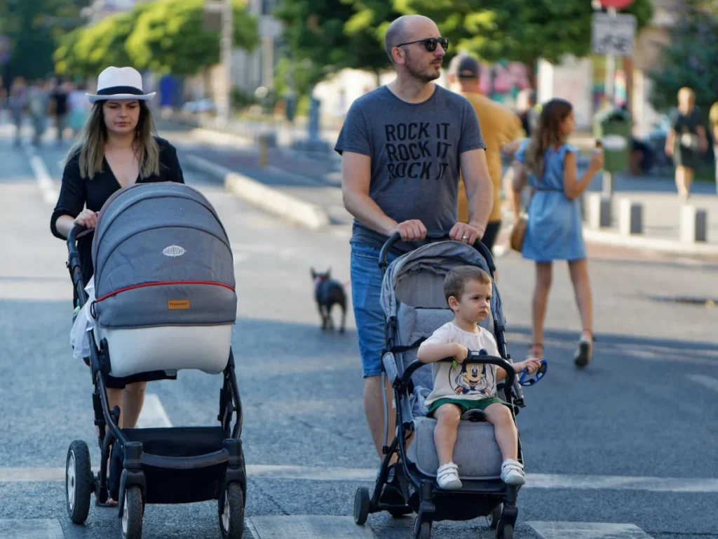 Family walking together with strollers on a neighborhood street during summer.