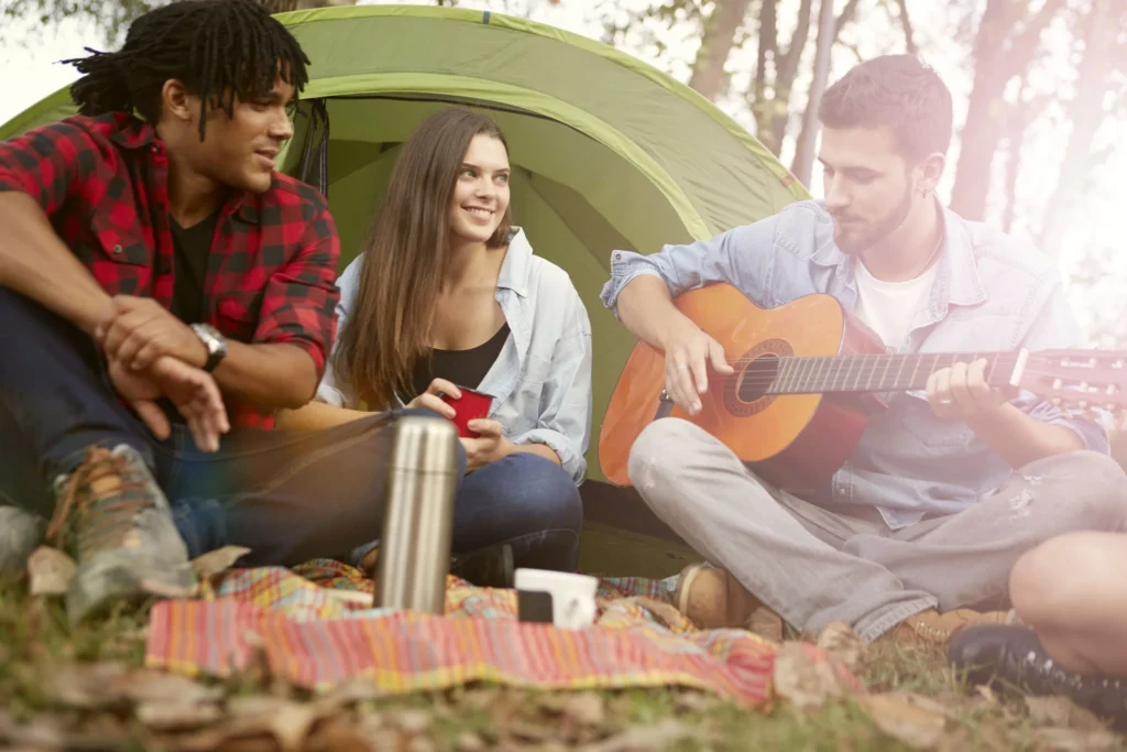 Friends sitting outside a tent and playing guitar during a camping trip.