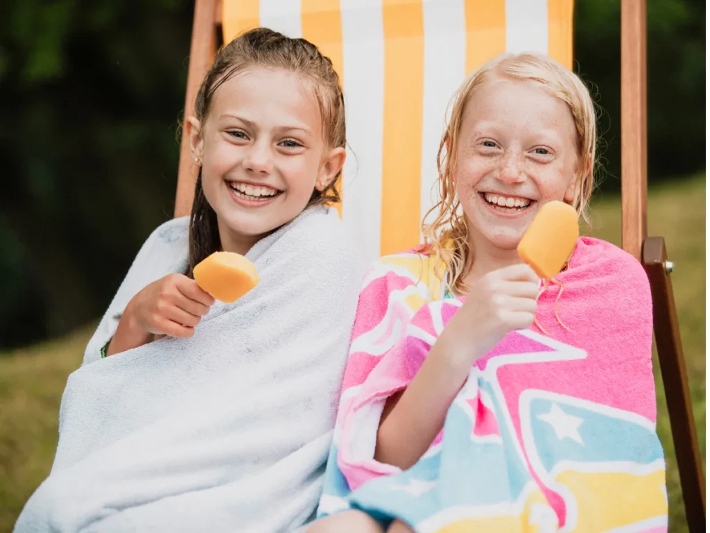 Two girls wrapped in towels enjoying popsicles outside on a warm summer day.