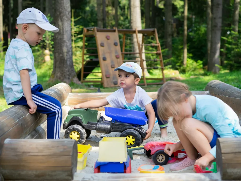 Children playing together with toy trucks and sand in an outdoor sandbox.