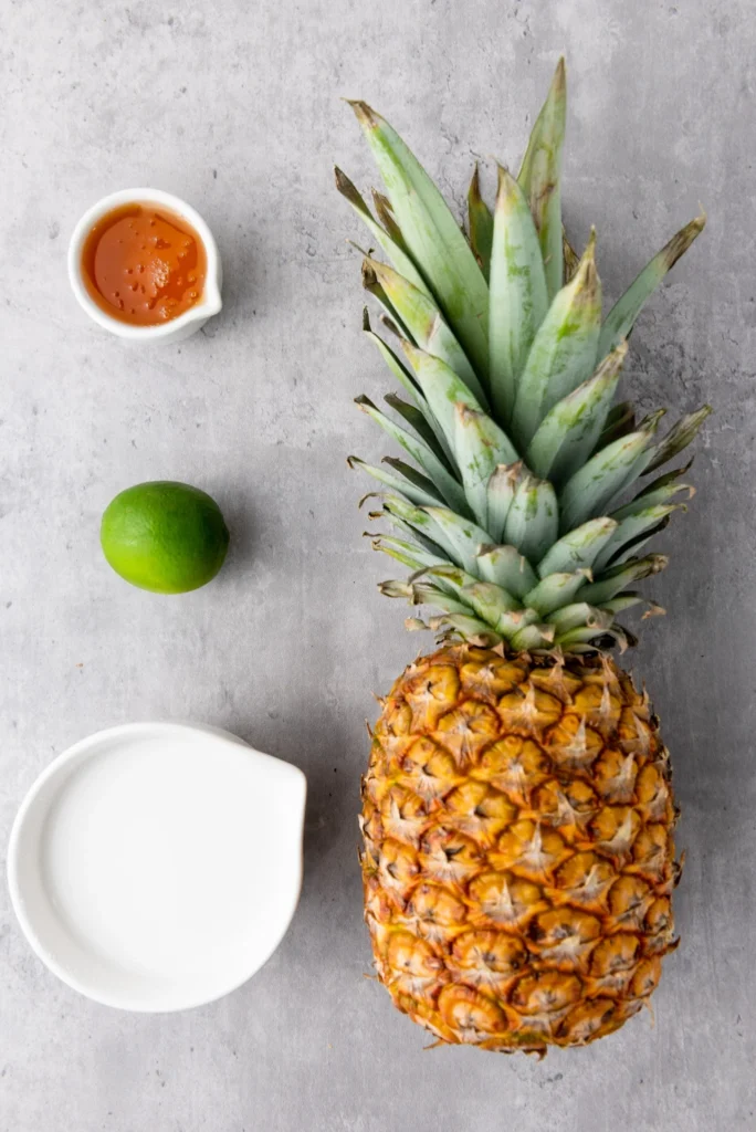 Fresh pineapple, coconut milk, lime, and honey arranged on a gray surface for pineapple coconut lime popsicles.