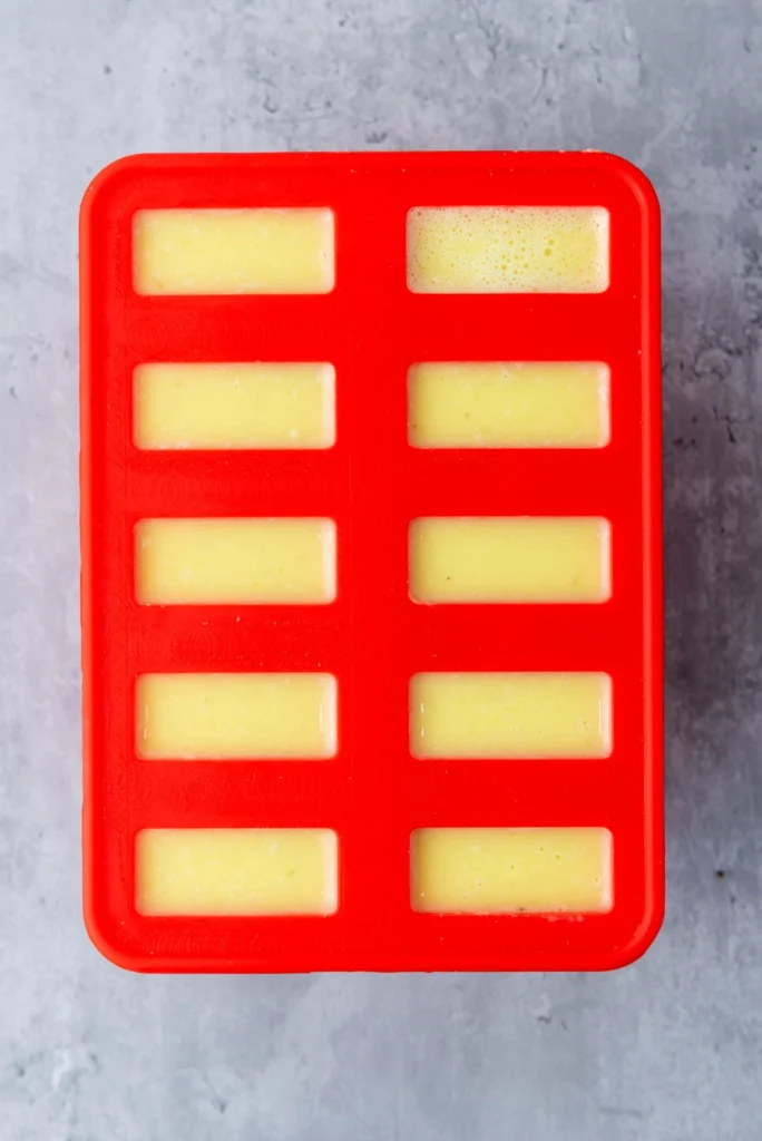 Pineapple coconut lime popsicle mixture poured into silicone molds before freezing.