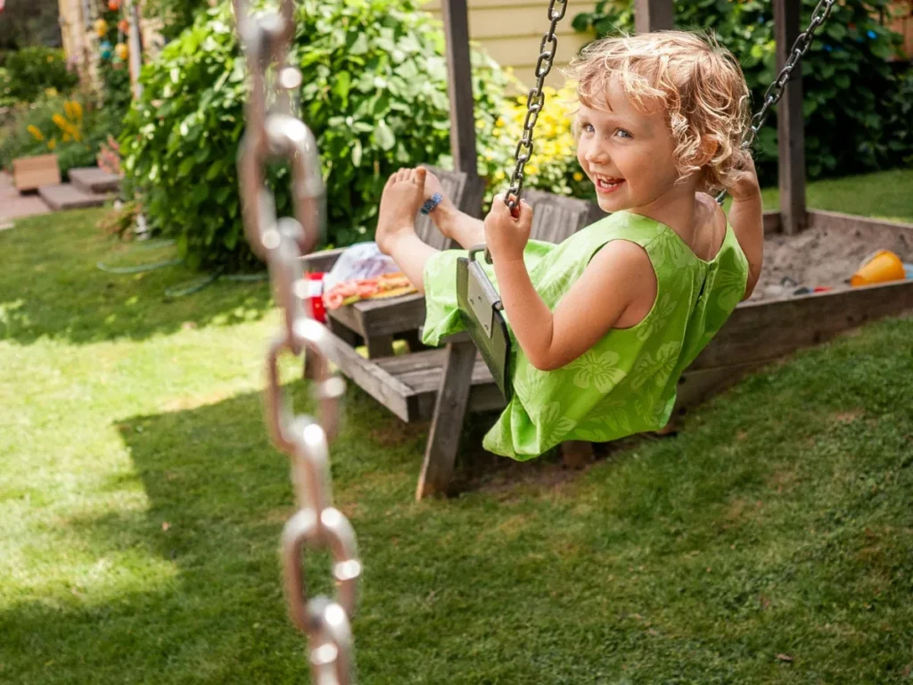 Young child smiling while swinging in a sunny backyard during summer.
