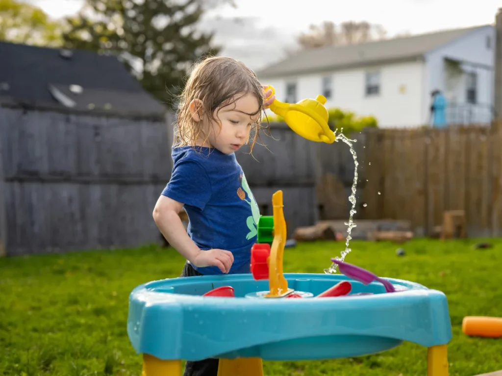 Toddler playing with a backyard water table on a warm summer afternoon.