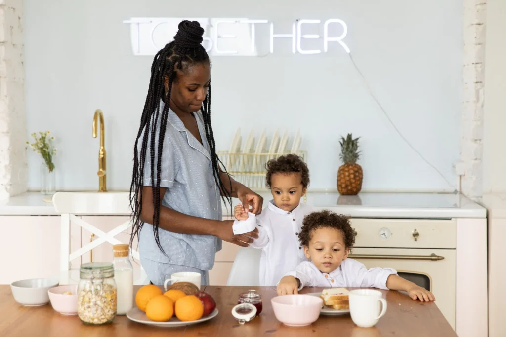 Mother helping two toddlers get ready for breakfast at the kitchen table.