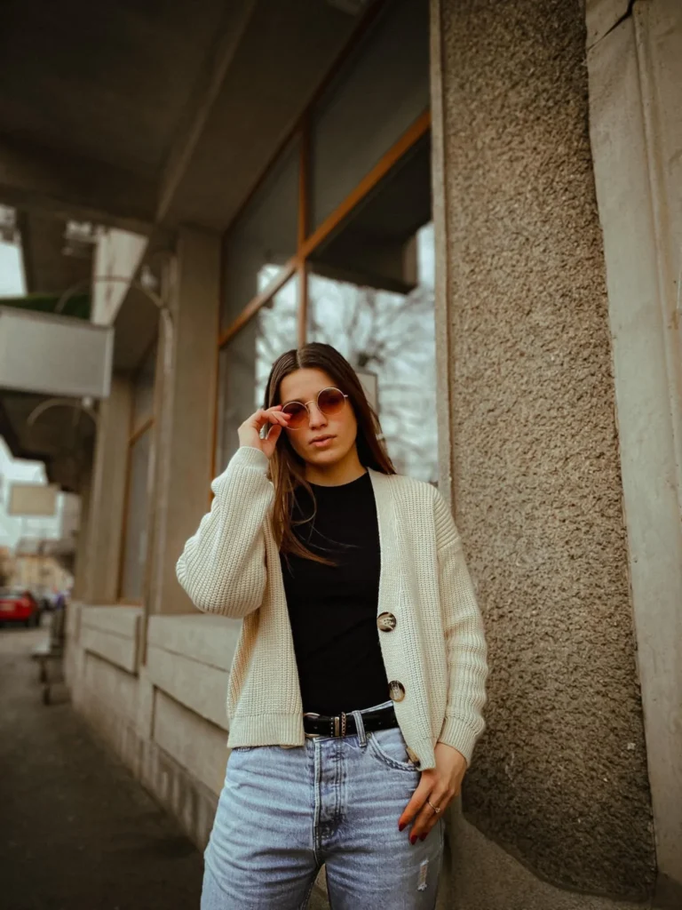 Woman wearing a cozy cream cardigan, black top, and jeans while standing outdoors on a city sidewalk.