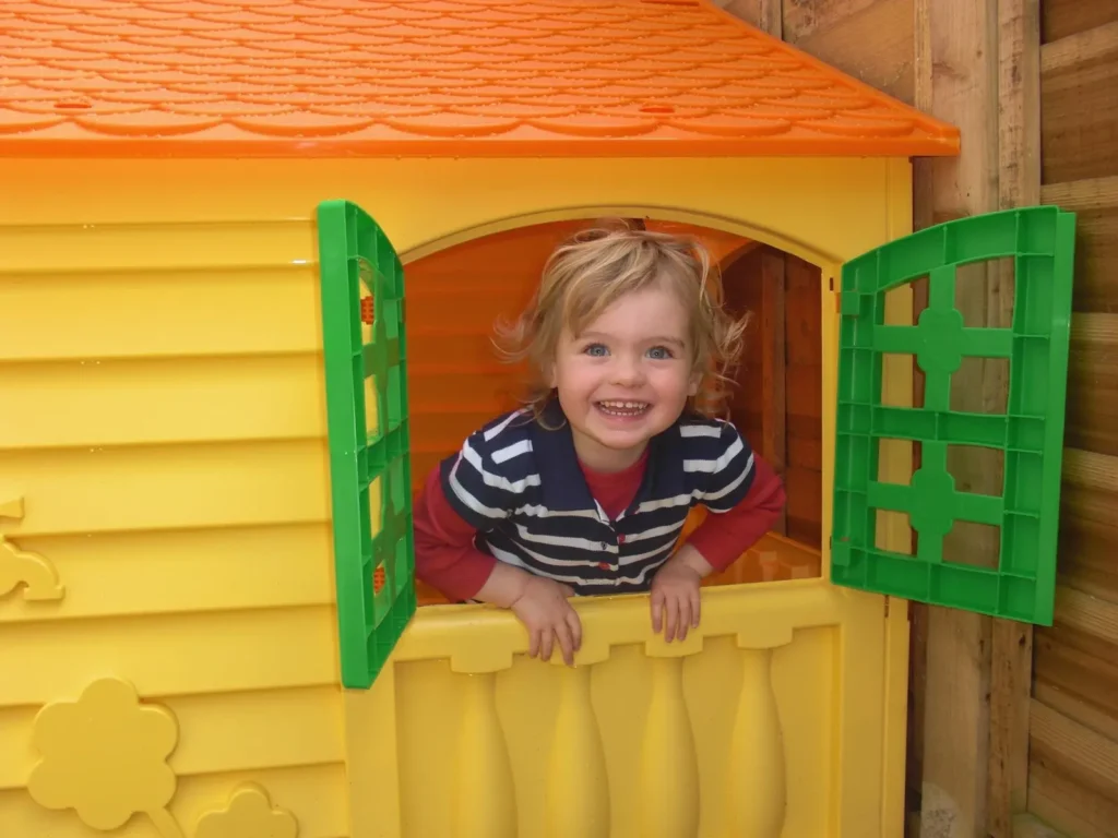 Smiling toddler looking through the window of a colorful outdoor playhouse