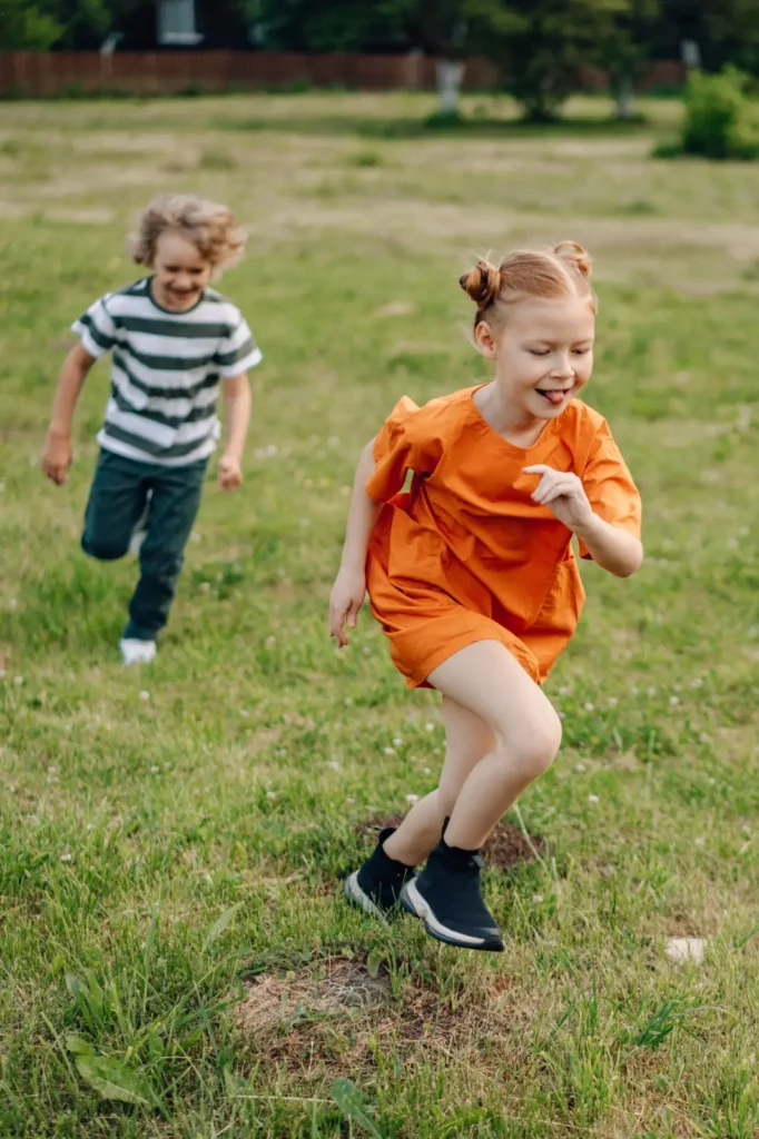 Two children running together across an open grassy play area