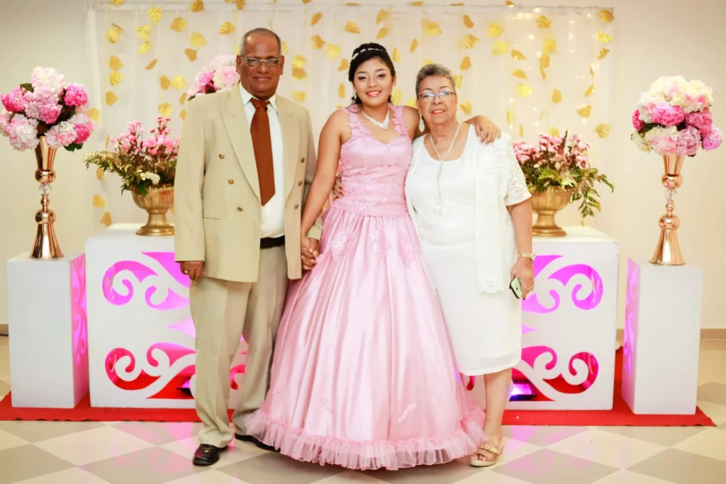 Young woman in a pink quinceañera dress standing with her grandparents