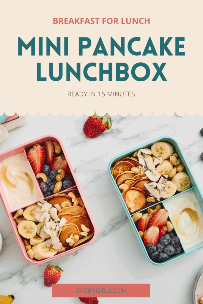 Two colorful breakfast lunchboxes filled with mini pancakes, yogurt, bananas, strawberries, blueberries, cashews, and coconut.
