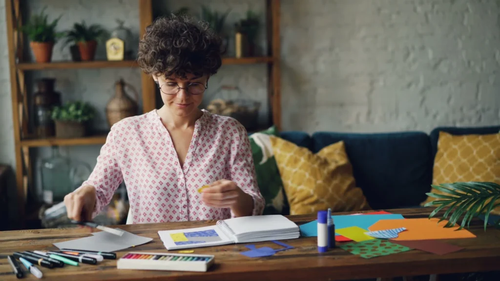 Woman making a paper craft at a large worktable in a comfortable, cozy room