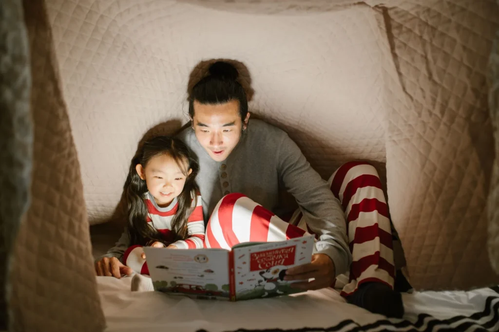 Father and daughter reading a book together inside a cozy blanket fort