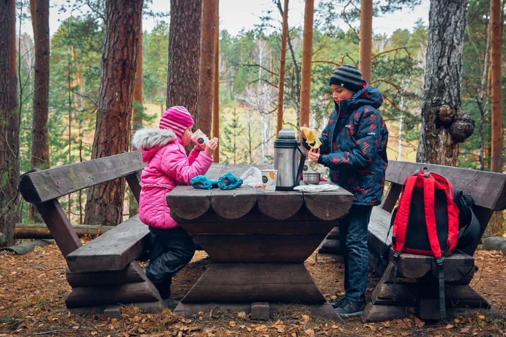 Bundled-up children enjoying warm drinks together at an outdoor picnic table