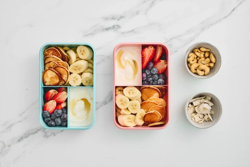 Mini pancake lunchboxes filled with bananas, strawberries, blueberries, yogurt, and honey