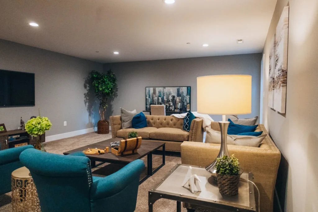 Comfortable finished basement family room with neutral sofas, teal armchairs, and coordinated decor.
