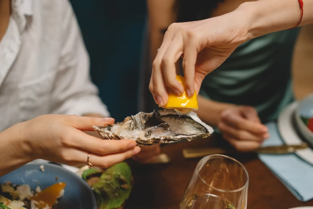 Guest squeezing fresh lemon over an oyster in its shell during a seafood dinner.
