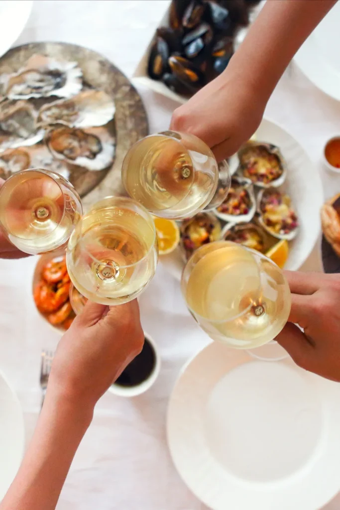 Dinner guests raising glasses of white wine in a toast over a seafood meal.
