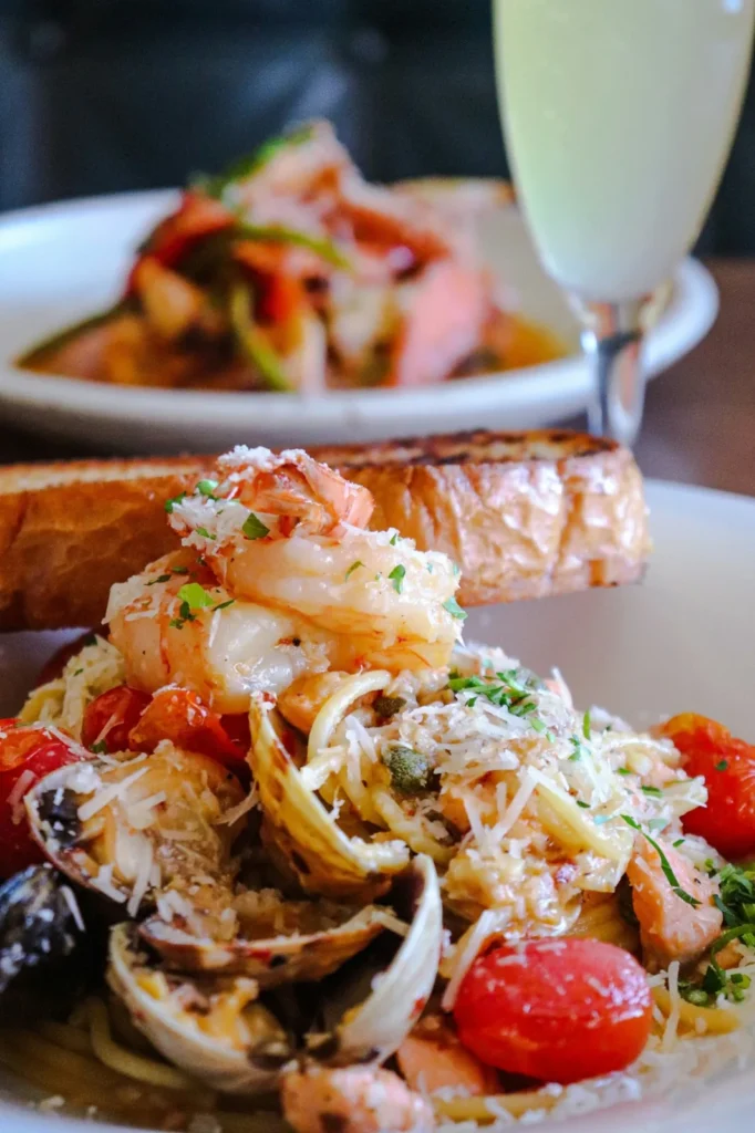 Seafood pasta topped with shrimp and shellfish, served with a glass of white wine.